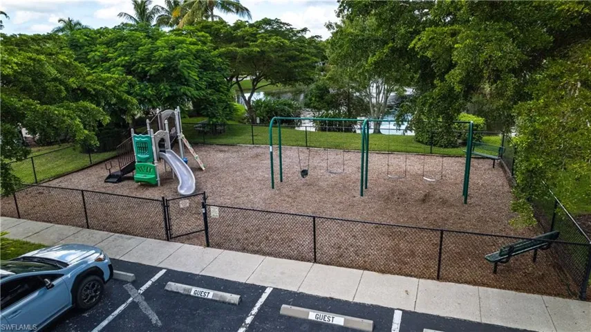 Fenced community playground featuring a playset with slides, swing sets, and a seating bench