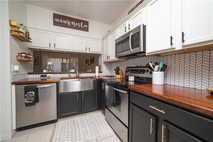 Stainless steel appliances, wood-finish countertops, herringbone tile backsplash, white upper cabinetry, and dark lower cabinetry
