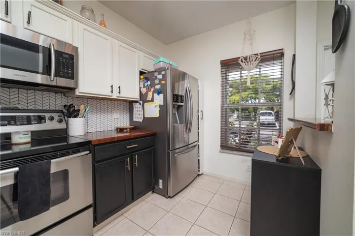 Modern kitchen featuring stainless steel appliances, two-tone cabinetry, a tile backsplash with a chevron pattern, and a window with wood blinds