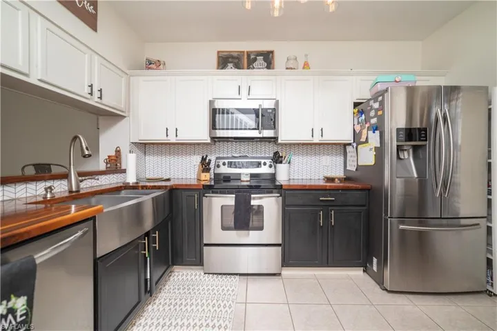 Kitchen featuring stainless steel appliances, wood-finish countertops, two-tone cabinetry, a farmhouse sink, and a patterned tile backsplash