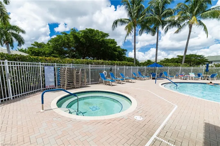 Outdoor pool with integrated hot tub, surrounded by paver decking, and secured with a perimeter fence