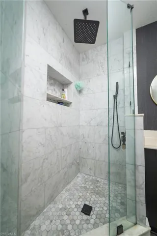 Shower featuring full-height stone tile walls, a rain showerhead, matte black fixtures, a recessed shower niche, and a hexagonal tile floor