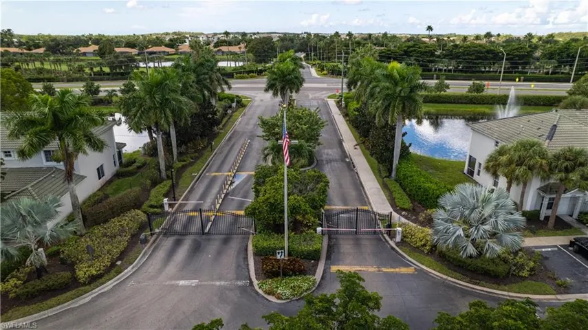Gated community entrance with a central median, mature palm trees, and a water feature with a fountain