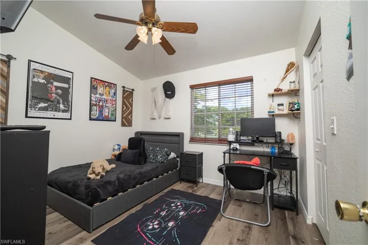 Vaulted ceiling with a ceiling fan, wood-finish flooring, and a window with blinds