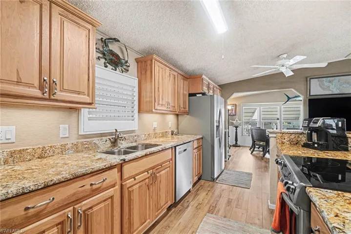 Kitchen with stainless steel appliances, light stone countertops, a ceiling fan, and light wood-style flooring