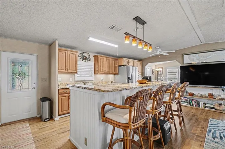 Kitchen featuring light stone countertops, a kitchen breakfast bar, light wood-style floors, stainless steel refrigerator with ice dispenser, and ceiling fan