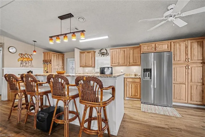 Kitchen featuring stainless steel fridge, a breakfast bar, decorative light fixtures, light stone countertops, and light wood-style flooring