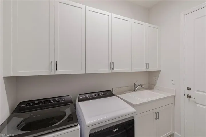 Clothes washing area featuring washing machine and clothes dryer, sink, and cabinets