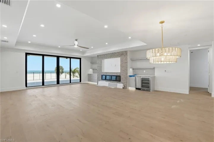 Unfurnished living room with light wood-type flooring, a stone fireplace, beverage cooler, a raised ceiling, and ceiling fan