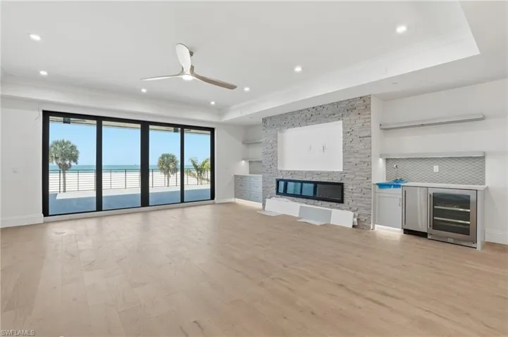 Unfurnished living room with ceiling fan, wine cooler, light wood-style flooring, ornamental molding, and a water view