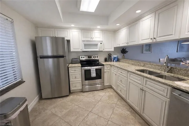 Kitchen with stainless steel appliances, recessed lighting, light stone counters, white cabinetry, and a raised ceiling