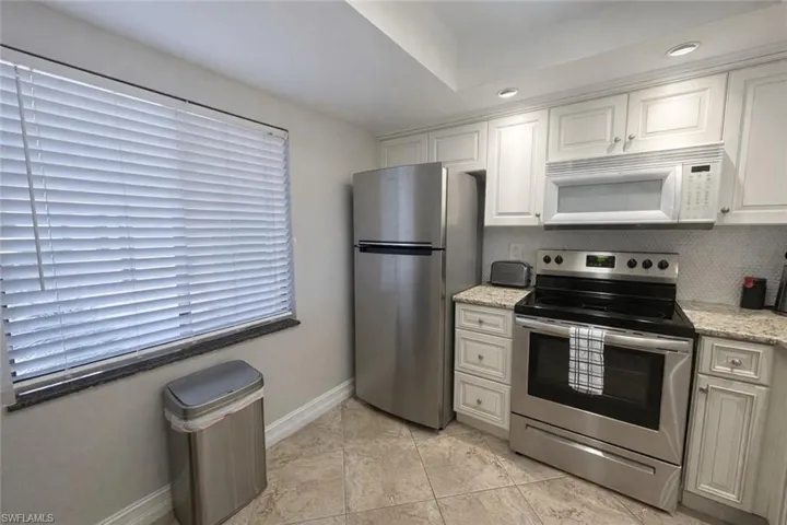 Kitchen featuring stainless steel appliances, white cabinets, light stone counters, and recessed lighting