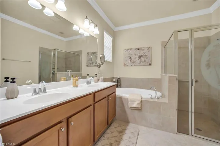 Bathroom featuring crown molding, a soaking tub, separate shower stall, double vanity