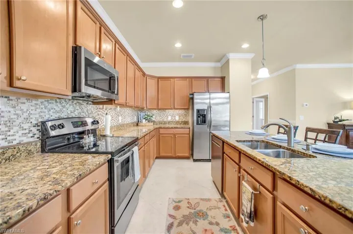Kitchen with stainless steel appliances, pendant lighting, backsplash,  stone counters, and crown molding