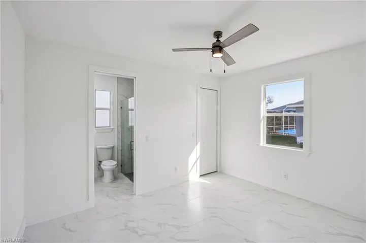 Unfurnished bedroom with a closet, ensuite bath, multiple windows, and ceiling fan