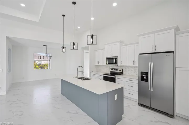 Kitchen featuring sink, an island with sink, appliances with stainless steel finishes, decorative light fixtures, and white cabinetry