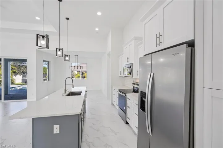 Kitchen featuring a kitchen island with sink, white cabinets, hanging light fixtures, sink, and appliances with stainless steel finishes