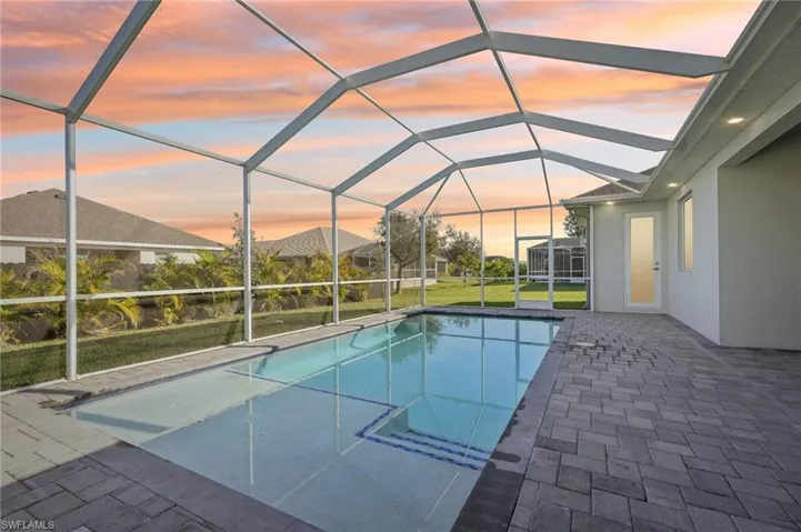 Pool at dusk with glass enclosure, a patio area, and a yard