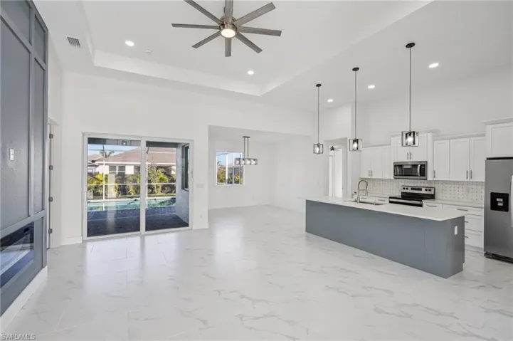 Kitchen with stainless steel appliances, ceiling fan, decorative light fixtures, white cabinets, and an island with sink