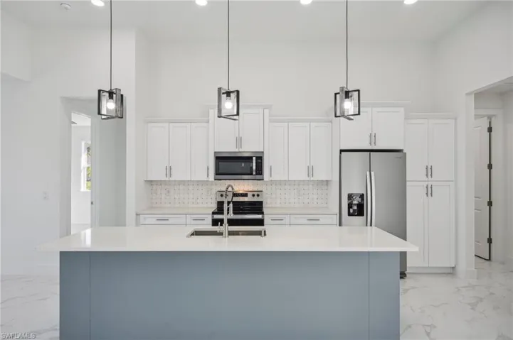 Kitchen featuring white cabinetry, an island with sink, decorative light fixtures, and appliances with stainless steel finishes