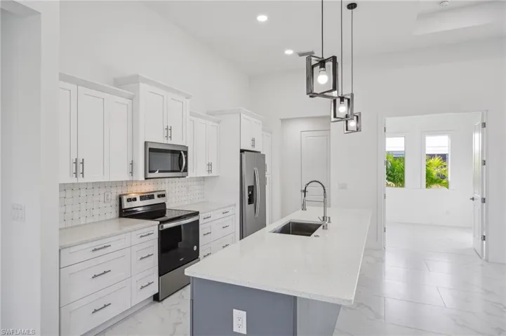 Kitchen with pendant lighting, a kitchen island with sink, white cabinets, sink, and appliances with stainless steel finishes