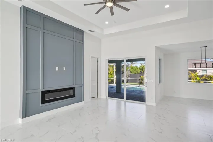Unfurnished living room featuring a raised ceiling, plenty of natural light, and ceiling fan