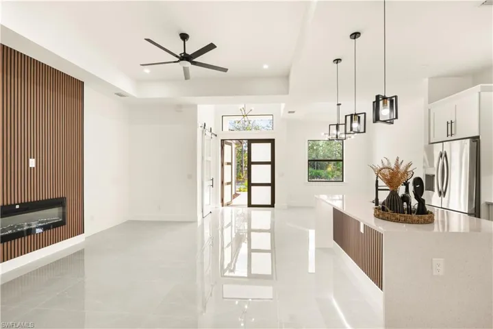 Kitchen with stainless steel fridge, hanging light fixtures, a kitchen island, light stone countertops, and white cabinets