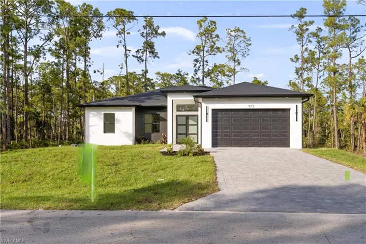 View of front facade featuring stucco siding, decorative driveway, a front yard, and an attached garage