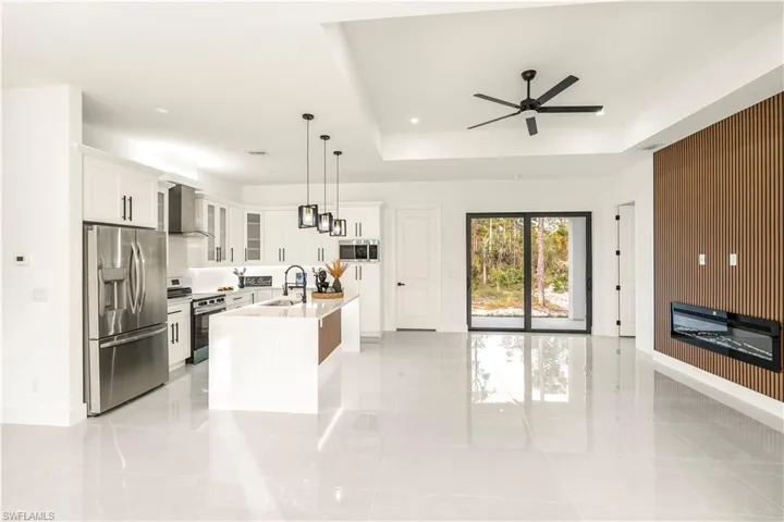 Kitchen with stainless steel appliances, glass insert cabinets, white cabinets, pendant lighting, and an island with sink