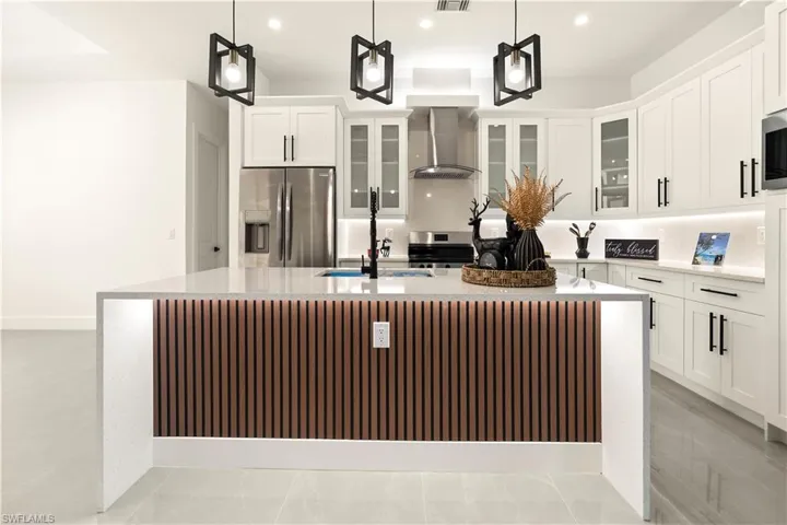 Kitchen with a large island, appliances with stainless steel finishes, light stone counters, recessed lighting, and wall chimney exhaust hood