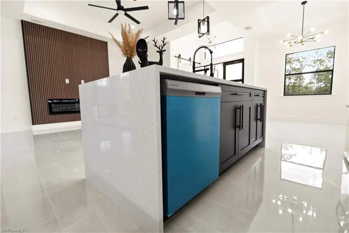 Kitchen with light tile patterned floors, a chandelier, dishwashing machine, decorative light fixtures, and light stone countertops