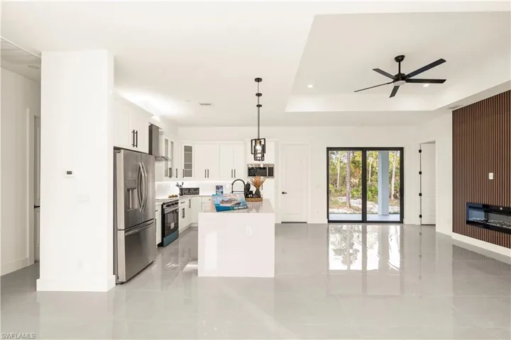 Kitchen featuring glass insert cabinets, stainless steel appliances, decorative light fixtures, white cabinetry, and a kitchen island with sink