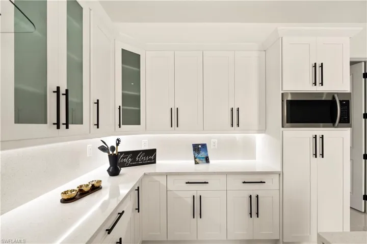 Kitchen featuring light stone counters, white cabinetry, stainless steel microwave, and glass insert cabinets
