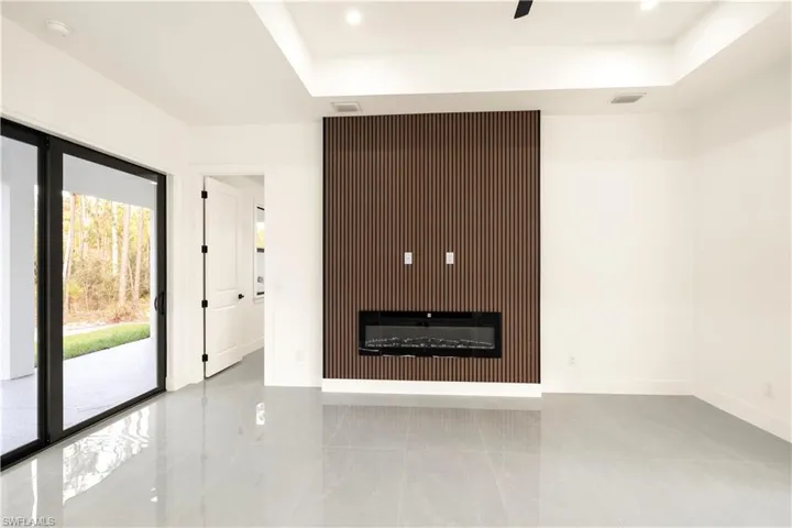 Unfurnished living room featuring a glass covered fireplace, a raised ceiling, light tile patterned floors, and recessed lighting