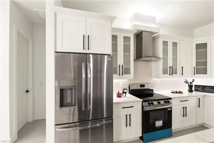 Kitchen featuring stainless steel appliances, white cabinets, wall chimney range hood, and light stone counters