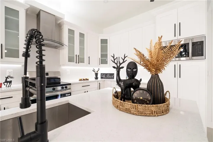 Kitchen featuring wall chimney exhaust hood, stainless steel appliances, light stone counters, white cabinets, and glass insert cabinets