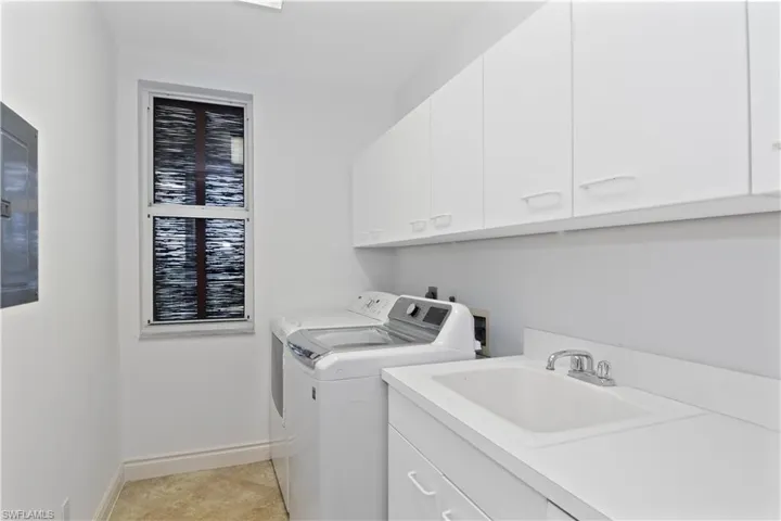 Laundry room with light tile patterned floors, sink, cabinets, and washer and dryer