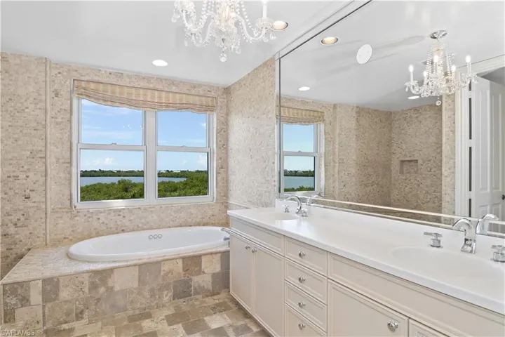 Bathroom featuring vanity, a relaxing tiled tub, a notable chandelier, and a water view