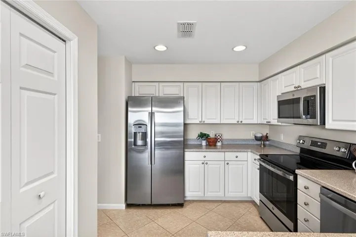 Kitchen with stainless steel appliances, white cabinetry, light tile patterned flooring, recessed lighting, and light stone counters