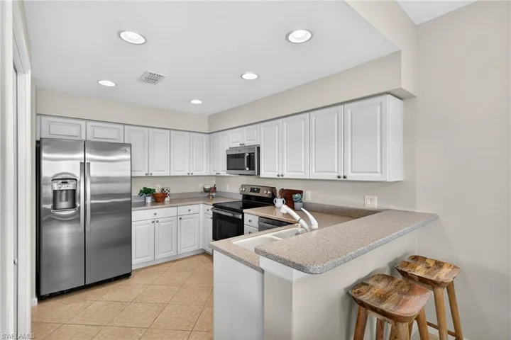 Kitchen with a peninsula, stainless steel appliances, white cabinets, a breakfast bar, and recessed lighting