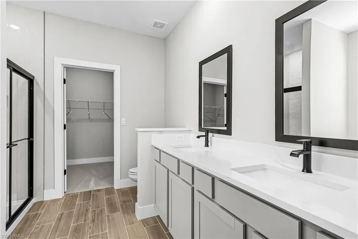 Bathroom with a walk in closet, double vanity, wood finish floors, and a shower with door