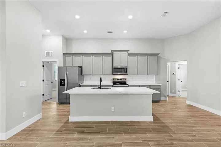 Kitchen featuring appliances with stainless steel finishes, gray cabinets, decorative backsplash, wood tiled floors, and a kitchen island with sink