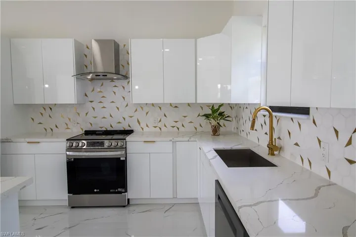 Kitchen with wall chimney exhaust hood, light stone counters, tasteful backsplash, stainless steel range, and white cabinets