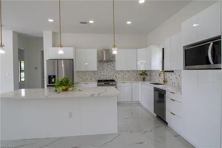 Kitchen with appliances with stainless steel finishes, wall chimney exhaust hood, decorative backsplash, light tile patterned floors, and white cabinets