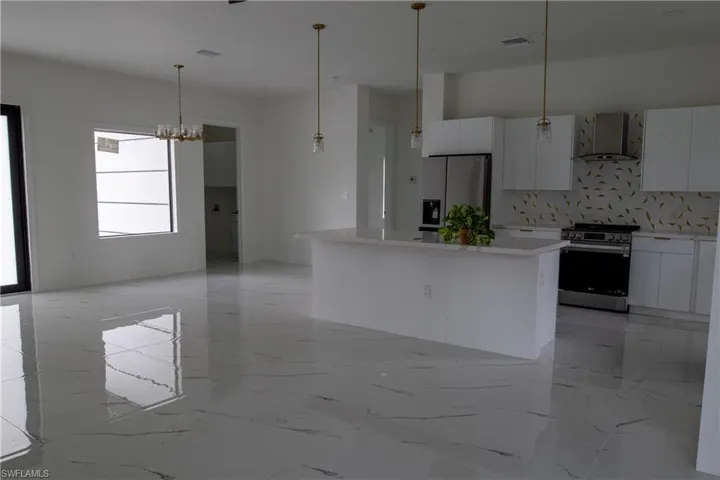 Kitchen with wall chimney range hood, decorative backsplash, a kitchen island, light tile patterned flooring, and stainless steel appliances