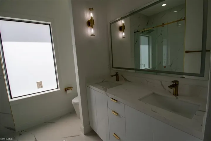 Bathroom featuring plenty of natural light, toilet, dual bowl vanity, and tile patterned floors