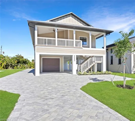 Beach home with decorative driveway, stairway, a front yard, an attached garage, and a carport