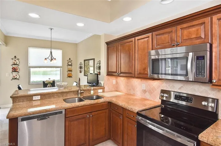 Kitchen featuring stainless steel appliances, a sink, crown molding, a peninsula, and brown cabinetry