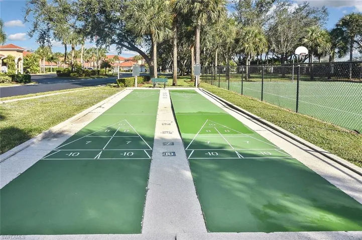View of home's community with a lawn, fence, and shuffleboard