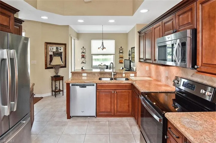 Kitchen featuring a sink, decorative backsplash, light tile patterned floors, stainless steel appliances, and a peninsula